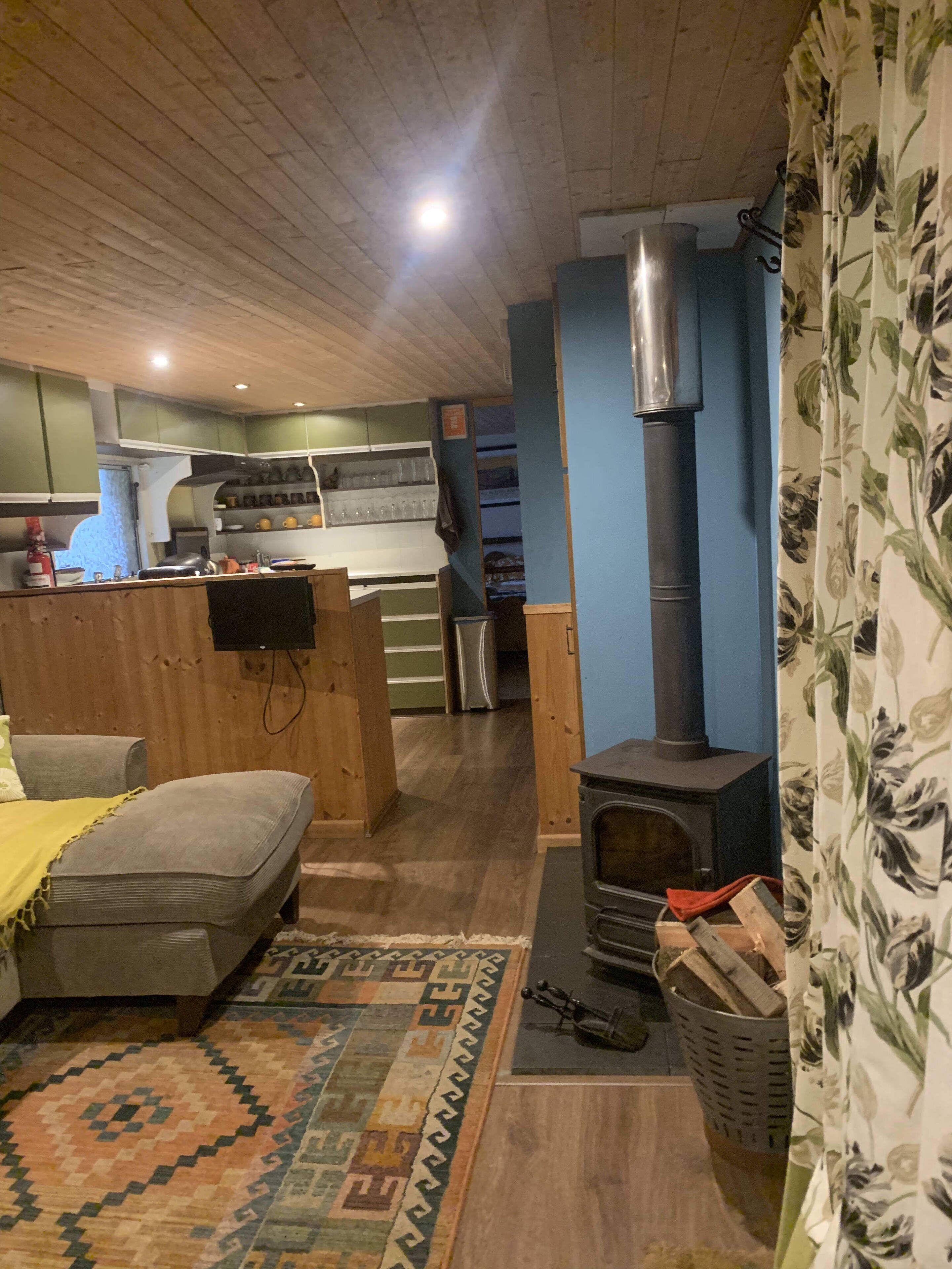 A cozy living room with a sofa, a patterned rug, a fireplace, and a kitchen area with wooden cabinets and a stove.