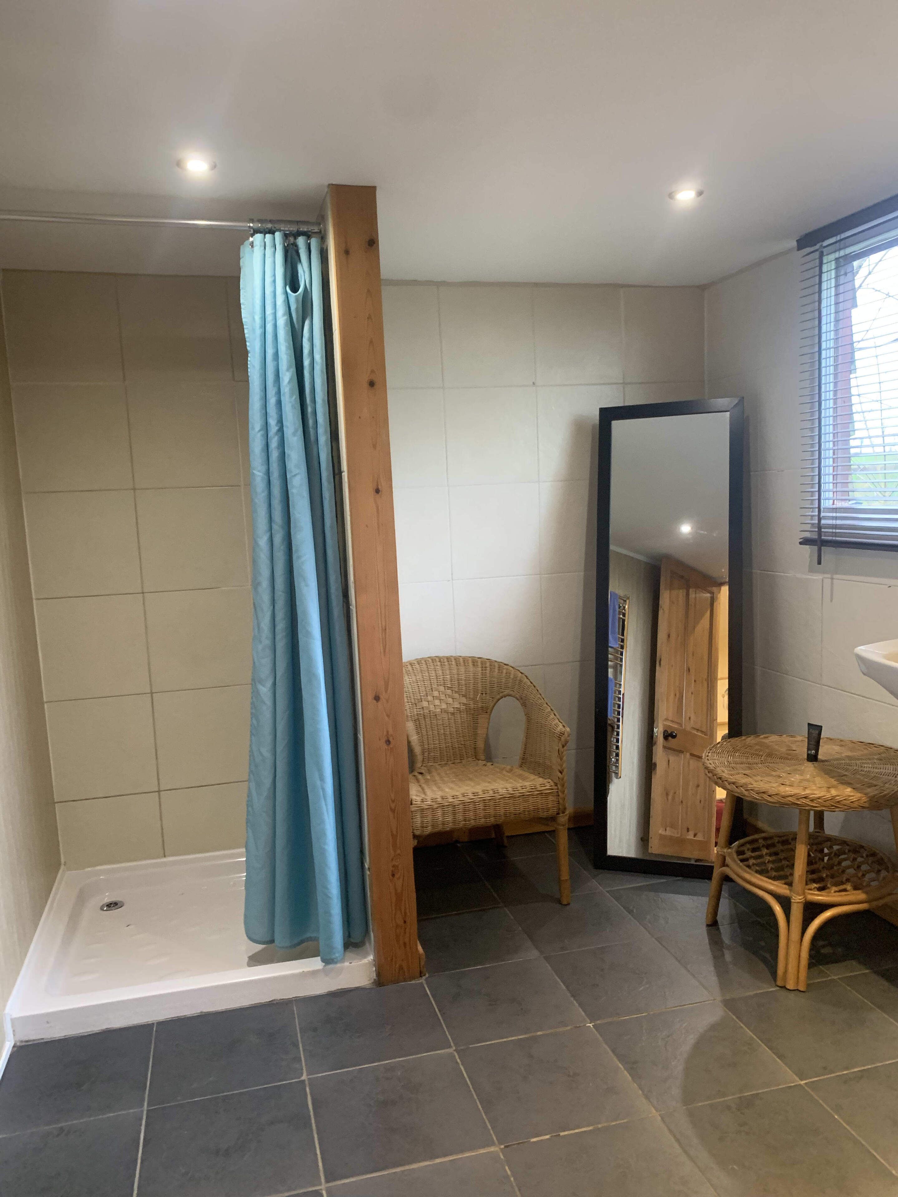 A bathroom with a shower, a wicker chair, a mirror, and a small round table.