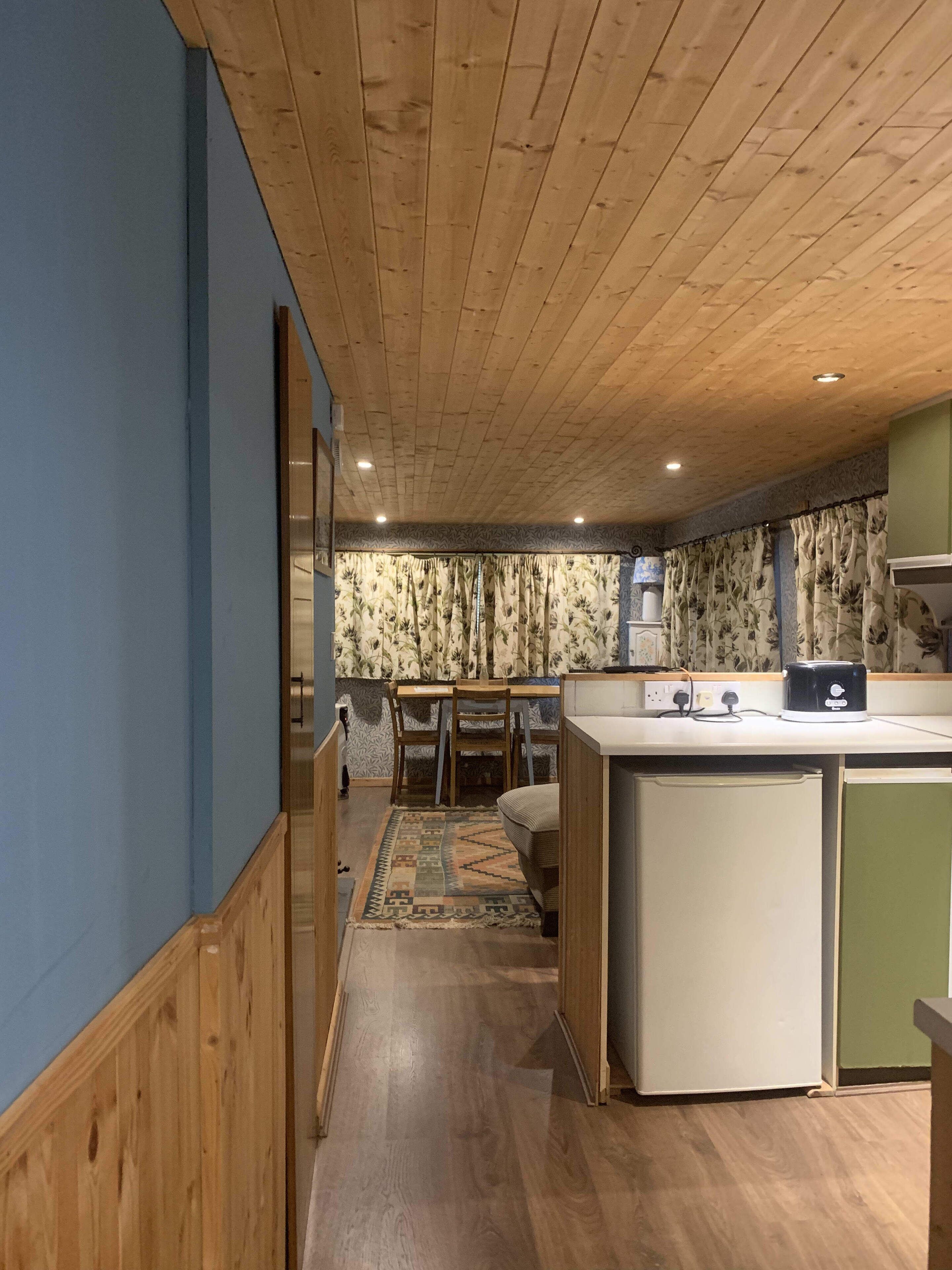 Una cocina moderna con techo de madera, un área de comedor con alfombra estampada y un refrigerador pequeño.