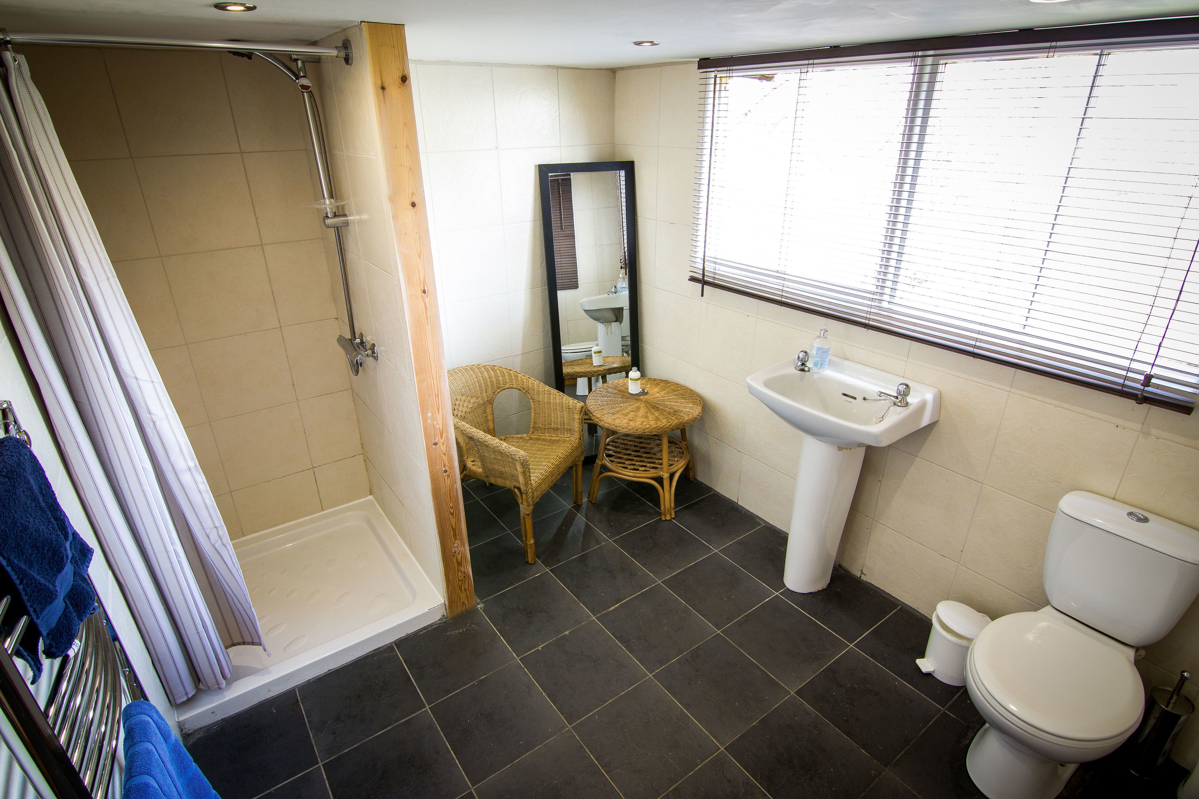 A bathroom with a shower, a sink, a toilet, wicker chairs, and a mirror.