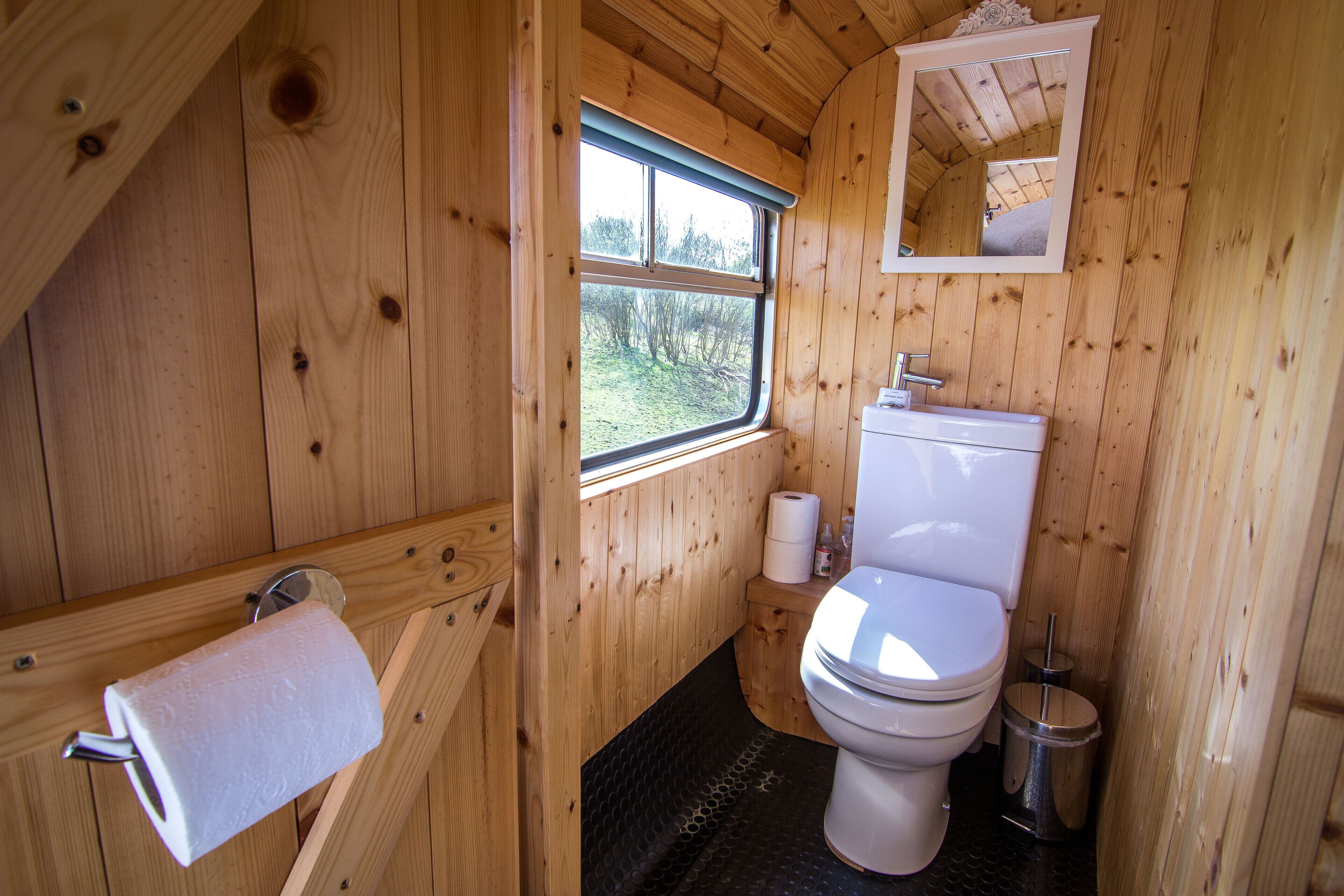 Ein Badezimmer einer Holzhütte mit Toilette, Waschbecken und Fenster.