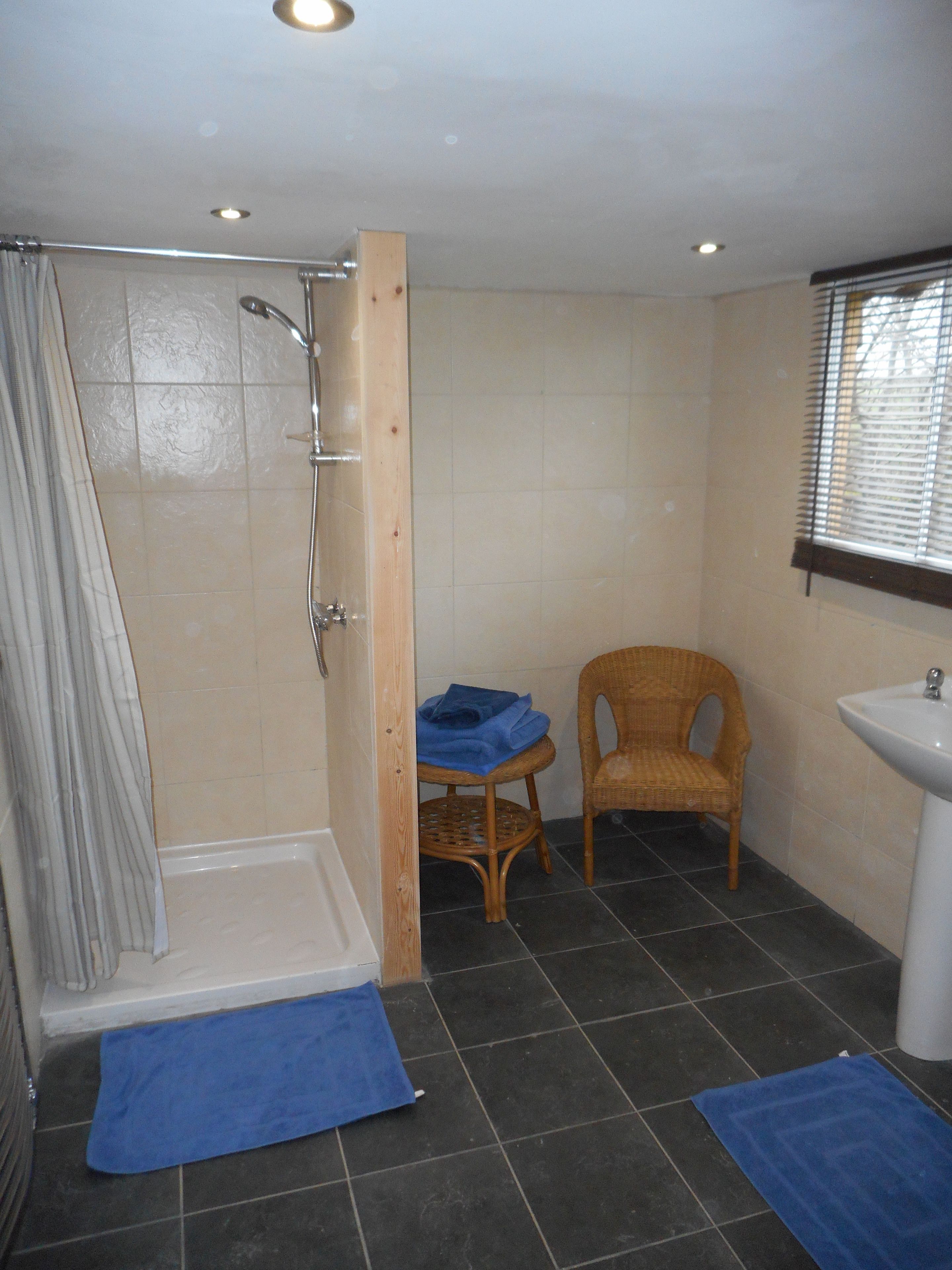 A bathroom with a shower, a sink, a chair, and a small table with towels.