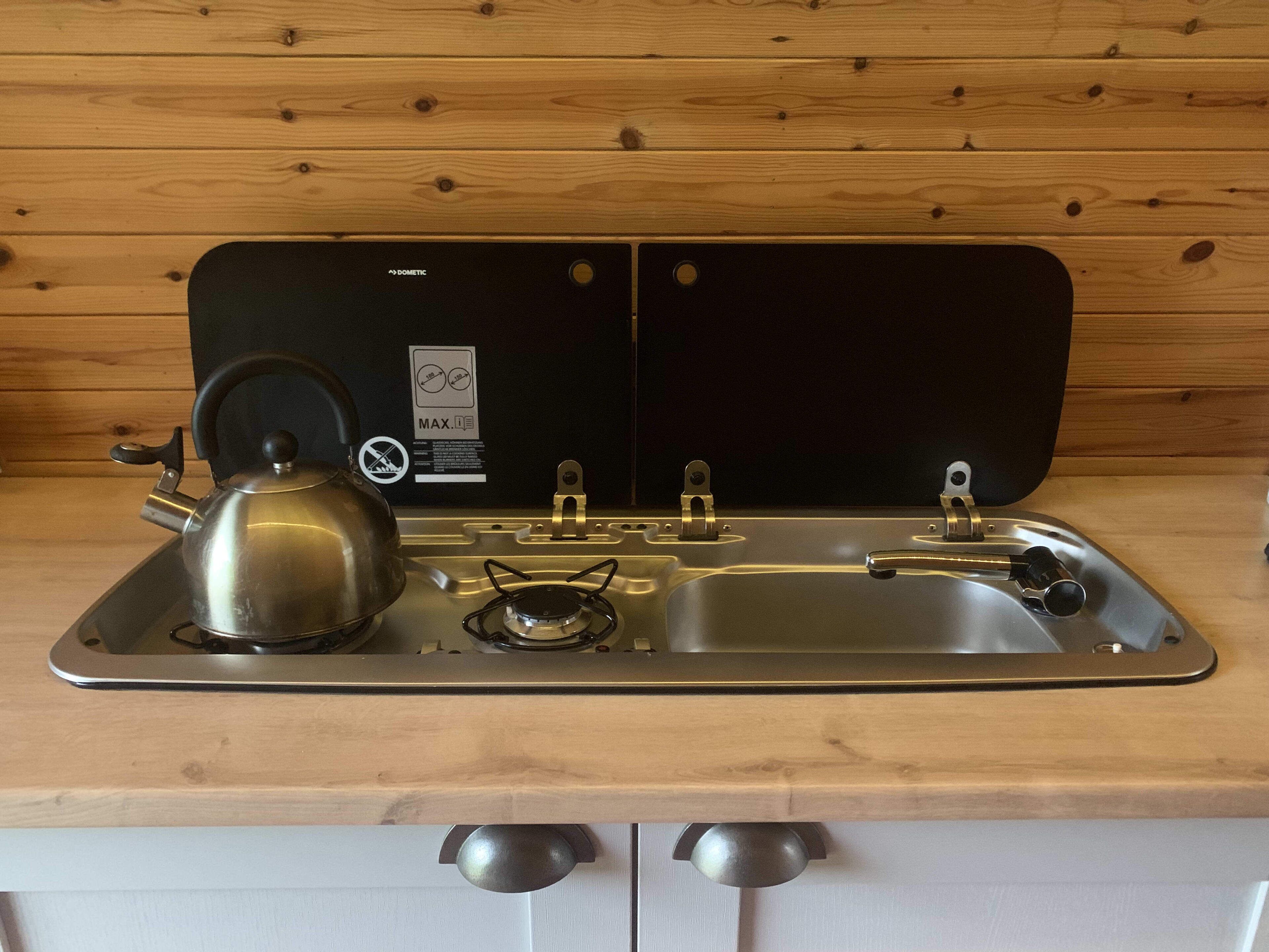 Una cocina con estufa de acero inoxidable, tetera y pileta.