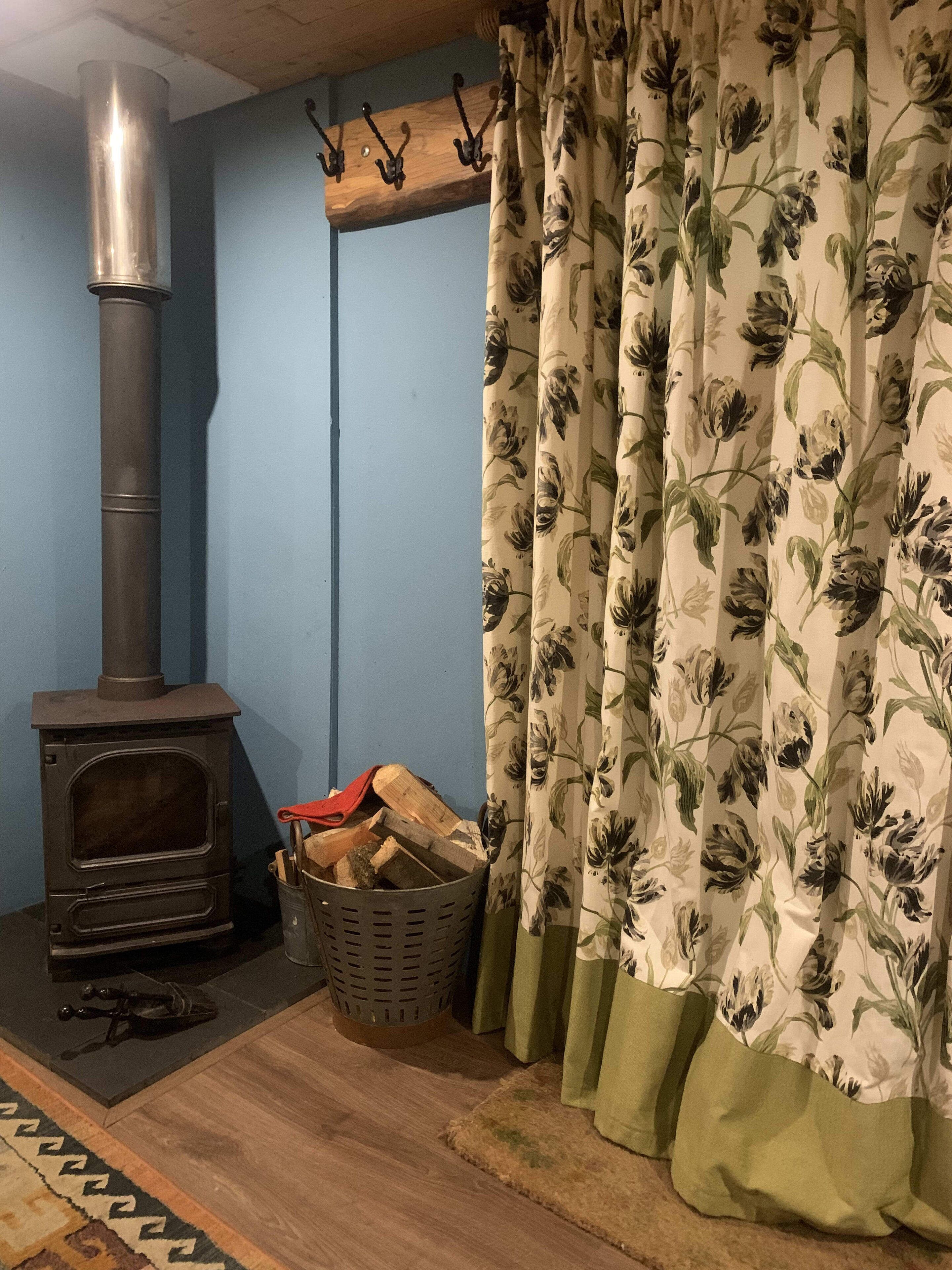 A room with a wood-burning stove, a basket of firewood, a patterned curtain, and a wooden floor.