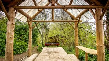 A wooden gazebo with a metal roof, surrounded by lush greenery.