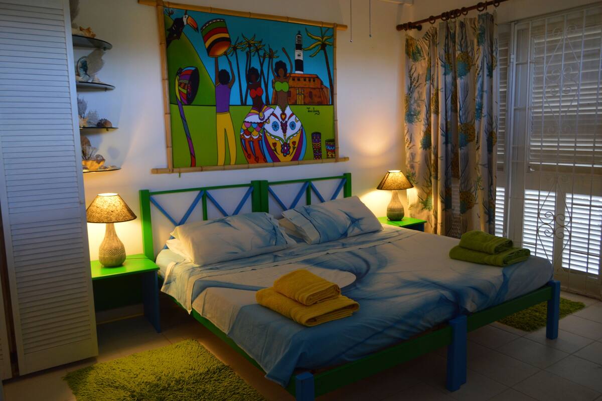 A bedroom with a bed, two nightstands, a painting, and a window with curtains.