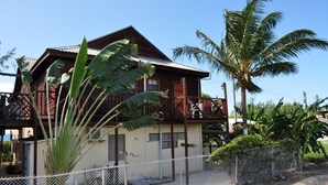 Ein zweistöckiges Holzhaus mit Balkon, umgeben von einem weißen Zaun und Palmen.