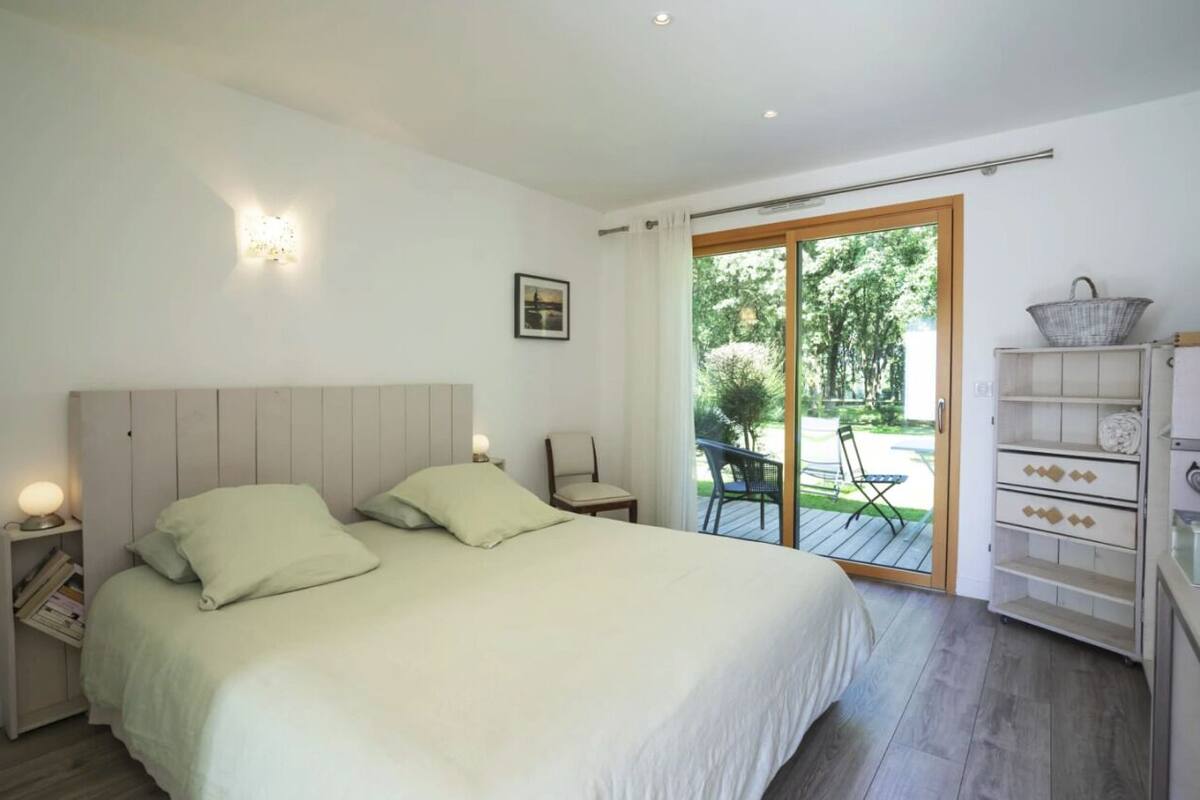 A bedroom with a large bed, a chair, a small table, and a bookshelf.