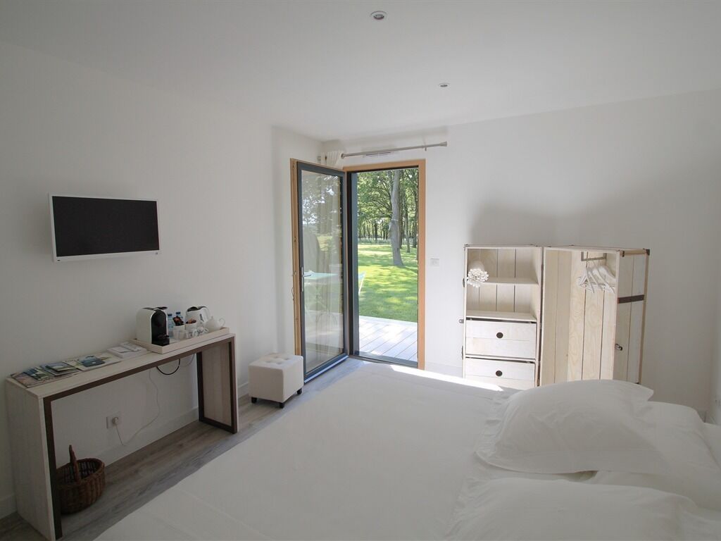 Un dormitorio moderno con una cama, un escritorio con una computadora, un televisor y un ventanal corredero a un jardín.