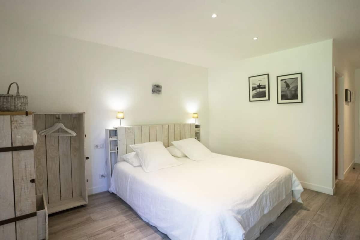 A bedroom with a wooden wardrobe, a bed with white linens, and two wall-mounted lamps.