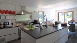 A modern kitchen with a large island, stainless steel appliances, and a view of the outdoors. - La Balade des Marais (Saint-Molf)