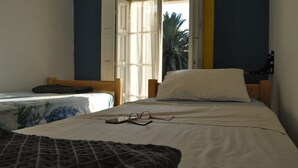 Un dormitorio con dos camas, una ventana con cortinas y vistas a palmeras afuera.
