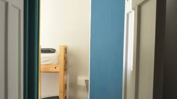 Un pasillo estrecho con una cama litera al fondo, una pared azul y una puerta cerrada.