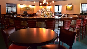 A bar area with a round table and multiple chairs, a well-stocked bar counter, and decorative wall art. - The Beaumont Inn (Dallas)
