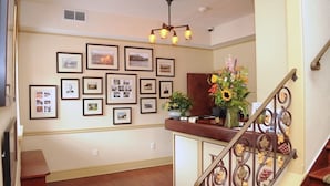 A hallway with framed photographs on the wall, a wooden bench, and a staircase with a decorative railing. - The Beaumont Inn (Dallas)