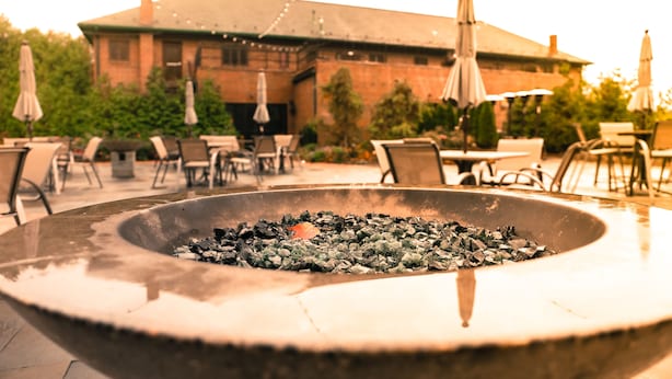 An outdoor seating area with a fire pit, tables, chairs, and umbrellas. - The Beaumont Inn (Dallas)
