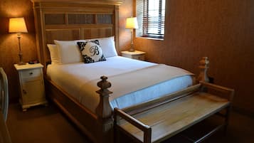 A neatly made bed with a wooden headboard, two bedside tables with lamps, and a window with blinds.