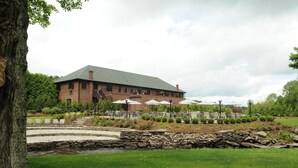 A large brick building with a green roof, outdoor seating area with umbrellas, and a stone water feature. - The Beaumont Inn (Dallas)