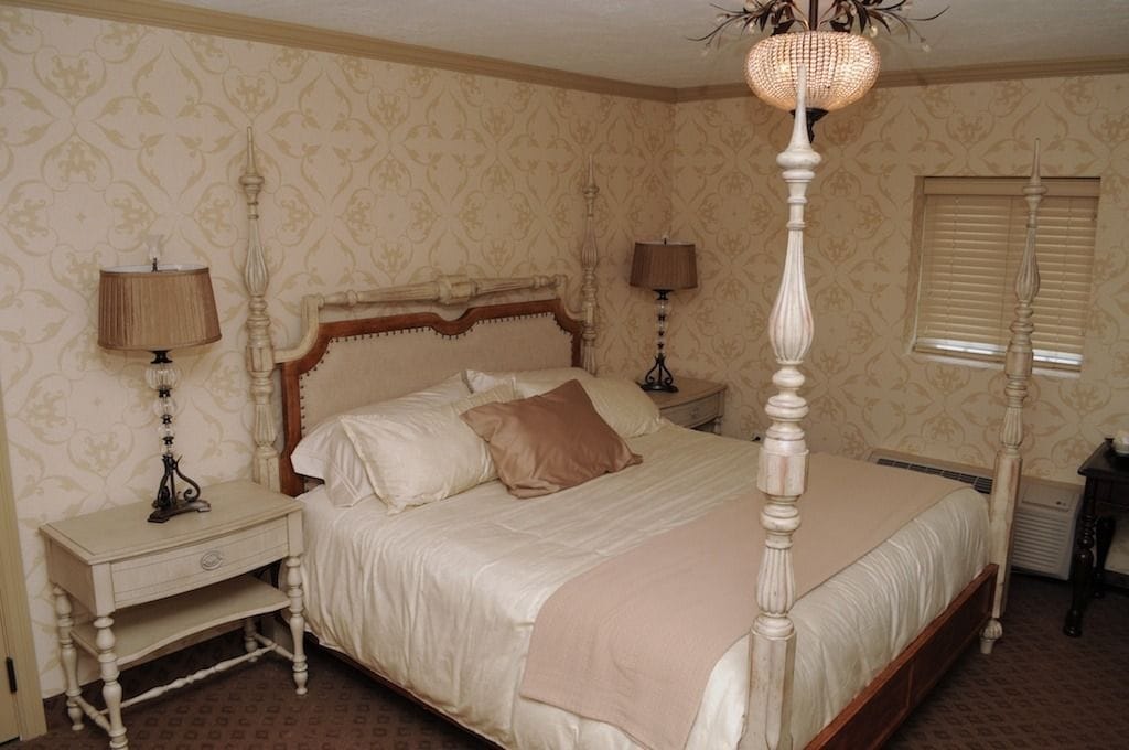 A classic four-poster bed with a wooden headboard, two bedside tables, and a lamp on each side.