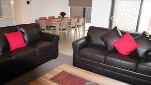 A living room with two dark brown leather sofas, each with a red pillow, and a wooden coffee table with a decorative plate. - Villa Waratah 19a/b/c (TULLAMARINE)