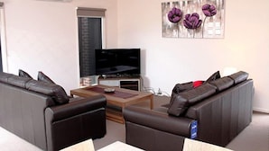 A living room with a sofa set, a coffee table, and a flat-screen TV. - Villa Waratah 19a/b/c (TULLAMARINE)