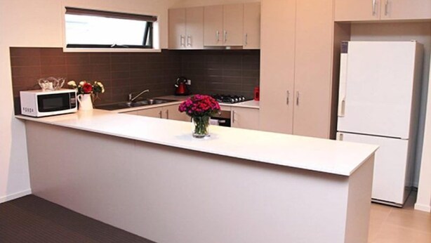 A modern kitchen with a white countertop, a microwave, a stove, and a refrigerator. - Villa Waratah 19a/b/c (TULLAMARINE)