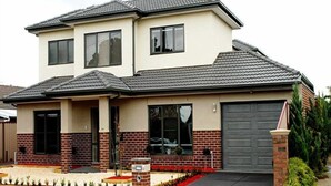 A two-story house with a garage, brick facade, and a small garden area with red flowers and white gravel. - Villa Waratah 19a/b/c (TULLAMARINE)