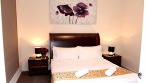A hotel room with a large bed, two bedside tables, and a wall-mounted artwork of purple flowers. - Villa Waratah 19a/b/c (TULLAMARINE)