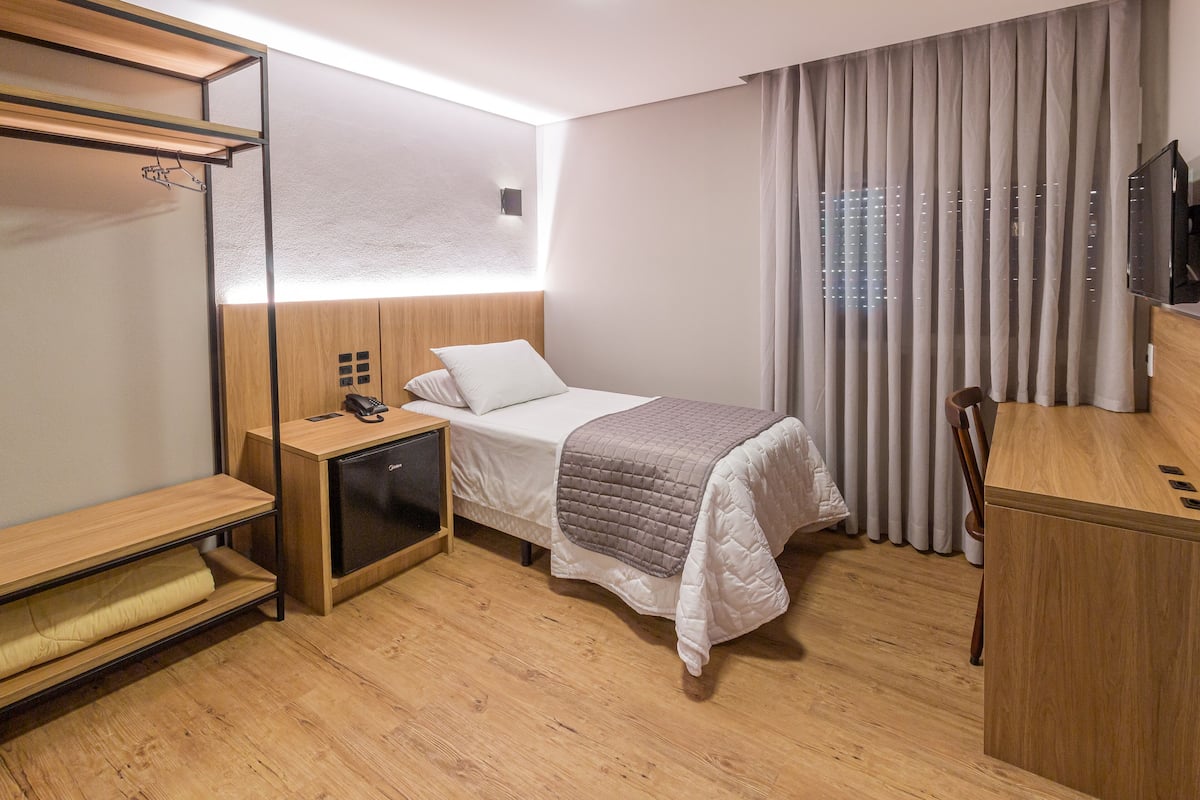 Une chambre d’hôtel de taille réduite, comprenant un lit, une table de chevet, un bureau, une chaise et un téléviseur.