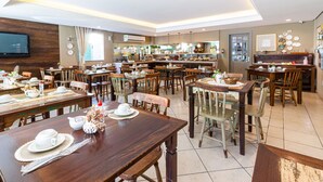 A spacious dining area with multiple tables and chairs, a kitchen in the background, and a flat-screen TV mounted on the wall. - Hotel Werlich (Sao Jose)
