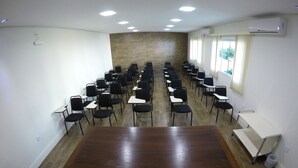 A conference room with rows of chairs and tables, a wooden accent wall, and an air conditioning unit. - Hotel Werlich (Sao Jose)