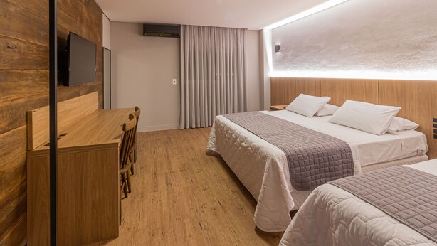 A modern hotel room with a wooden desk, two beds, and a large window with curtains. - Hotel Werlich (Sao Jose)