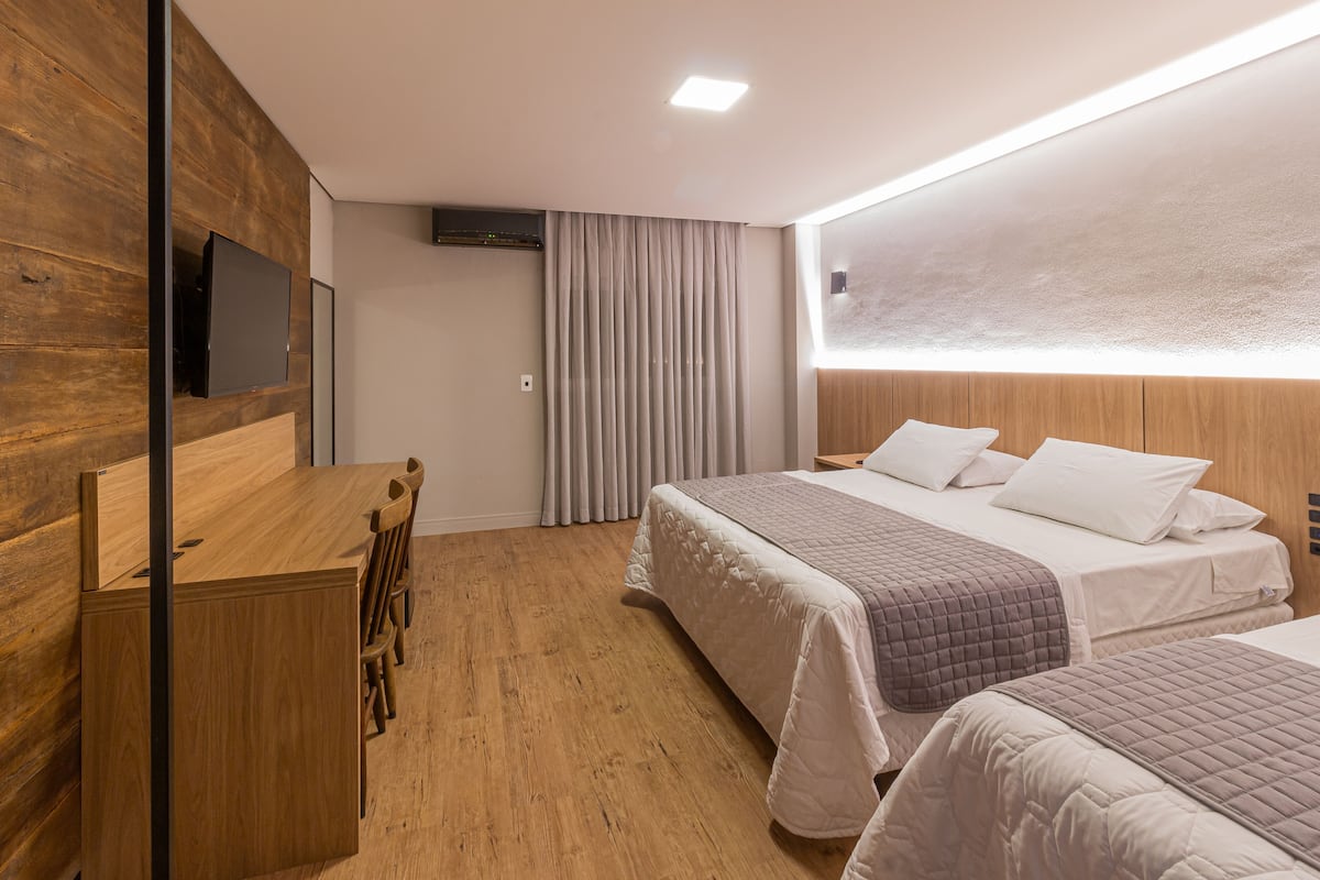 Une chambre d’hôtel moderne avec un bureau en bois, deux lits et une grande fenêtre avec des rideaux.