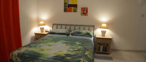 Un dormitorio con una cama, dos mesitas de noche con lámparas, una cortina roja y tres obras de arte colgadas en la pared.