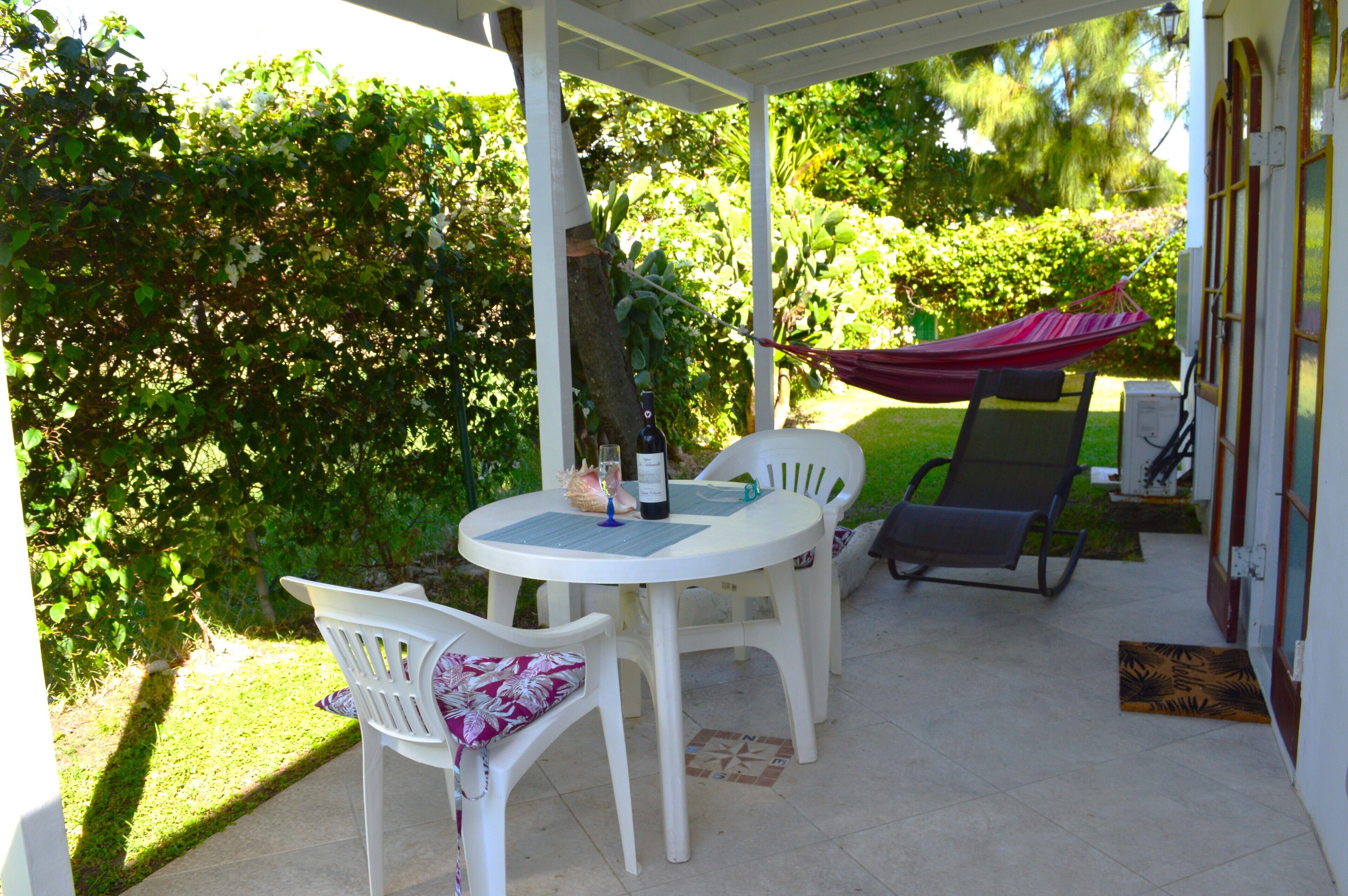 Eine überdachte Terrasse mit Tisch und Stühlen, einer Hängematte und üppigem Grün.