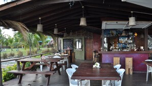 Een terras met houten tafels en witte stoelen, een bar met verschillende flessen en een krijtbordmenu.