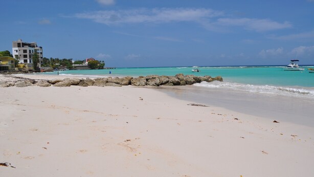 Een strand met helder turquoise water, een rotsenrij en enkele boten.