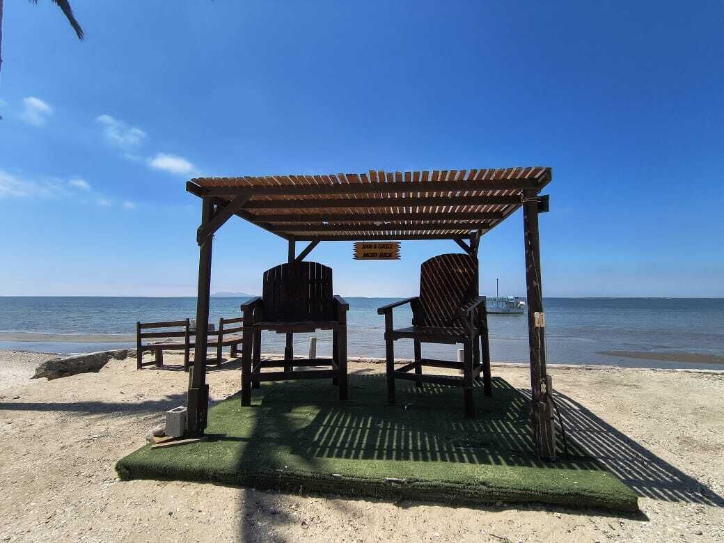 Una playa con un pabellón de madera, dos sillas y una pequeña mesa.