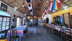 A restaurant with a rustic interior, wooden tables, a bar area, and various flags hanging from the ceiling. - Hotel Villas Mar y Arena (Comondu)