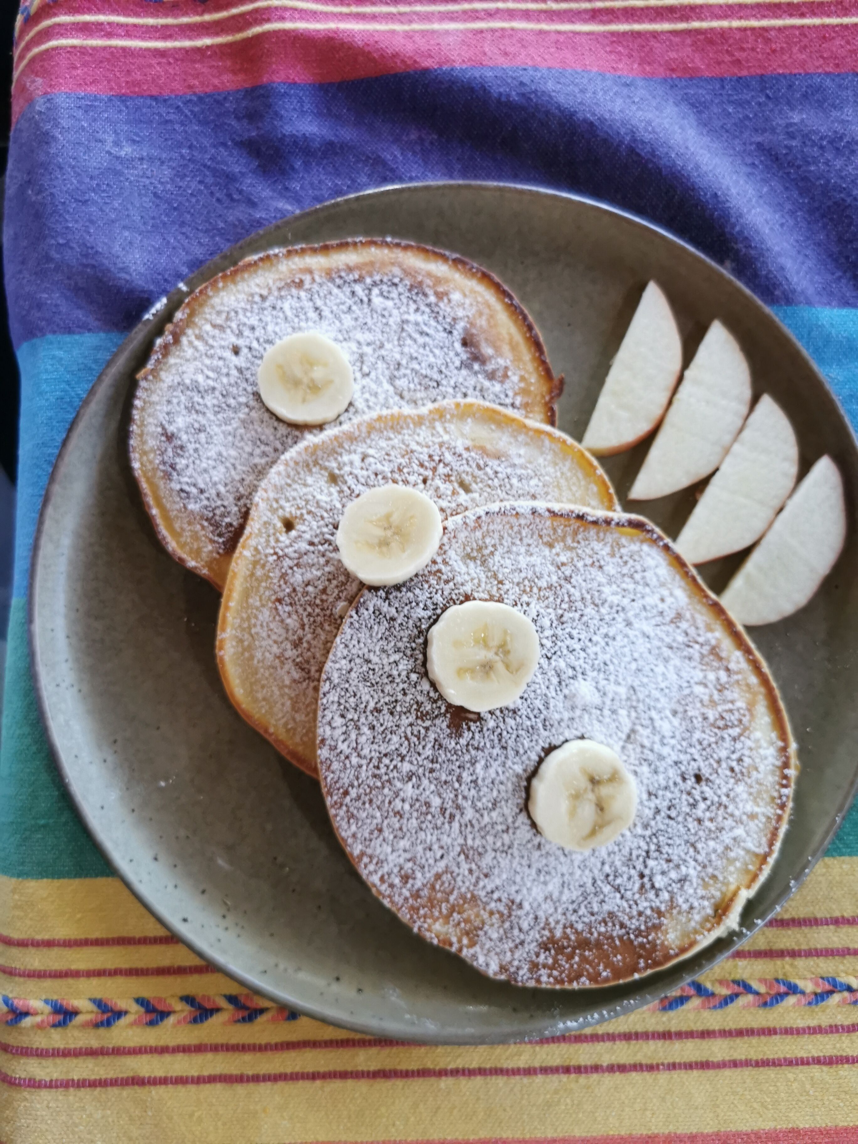 Une assiette de crêpes garnies de tranches de banane et saupoudrées de sucre glace.