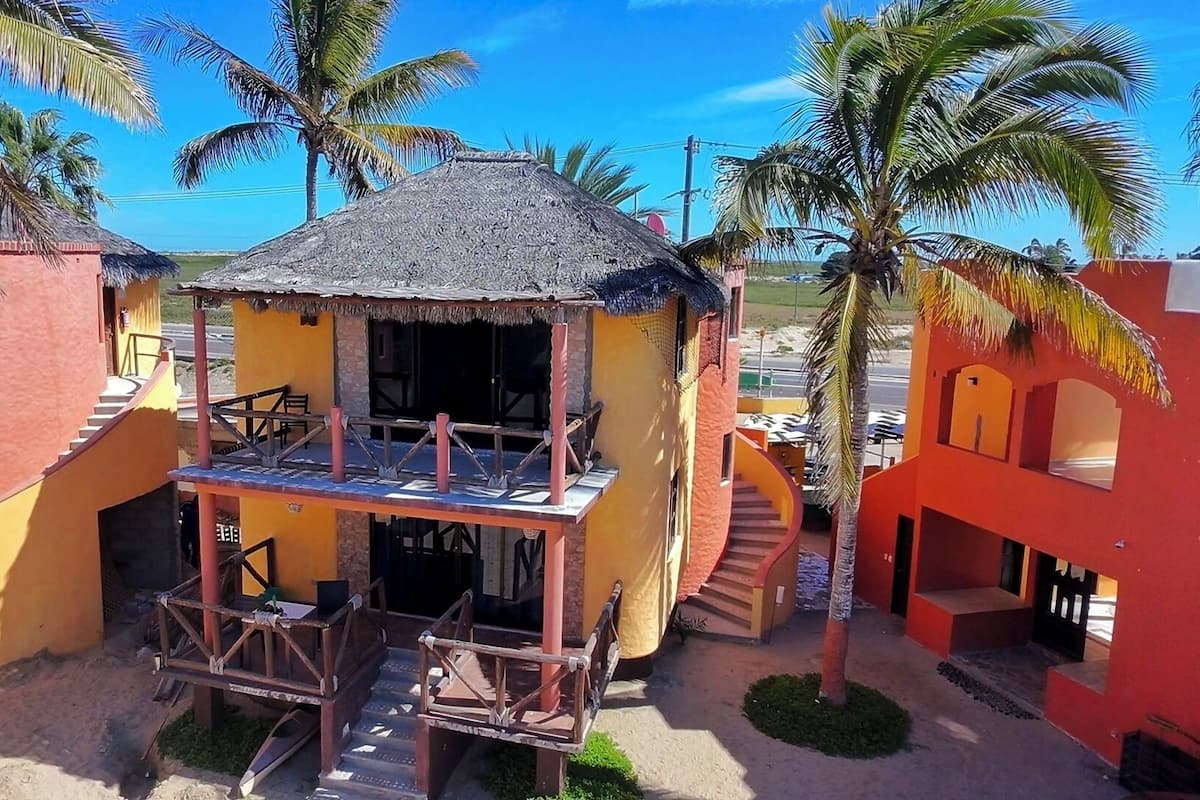 A small, colorful building with a thatched roof, a staircase, and a wooden deck.