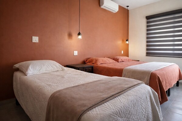 A hotel room with two beds, a nightstand, a wall-mounted air conditioner, and a window with blinds. - Hotel Villas Mar y Arena (Comondu)