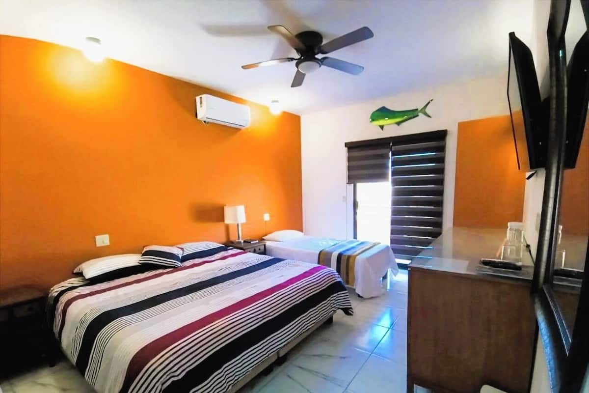 A hotel room with a bed, a desk, a chair, a ceiling fan, and a window with blinds.
