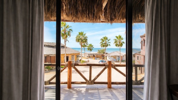 A balcony with a view of a beach, palm trees, and buildings. - Hotel Villas Mar y Arena (Comondu)