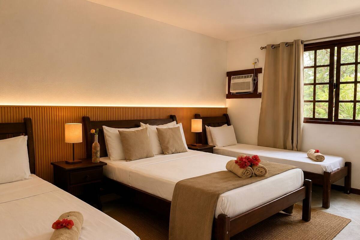 Une chambre d’hôtel avec deux lits simples, une tête de lit en bois, une table de chevet avec une lampe et une fenêtre avec des rideaux.