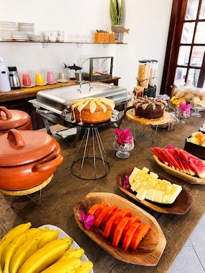 Buffet montado com diversos alimentos, um espaço para café e uma cozinha.