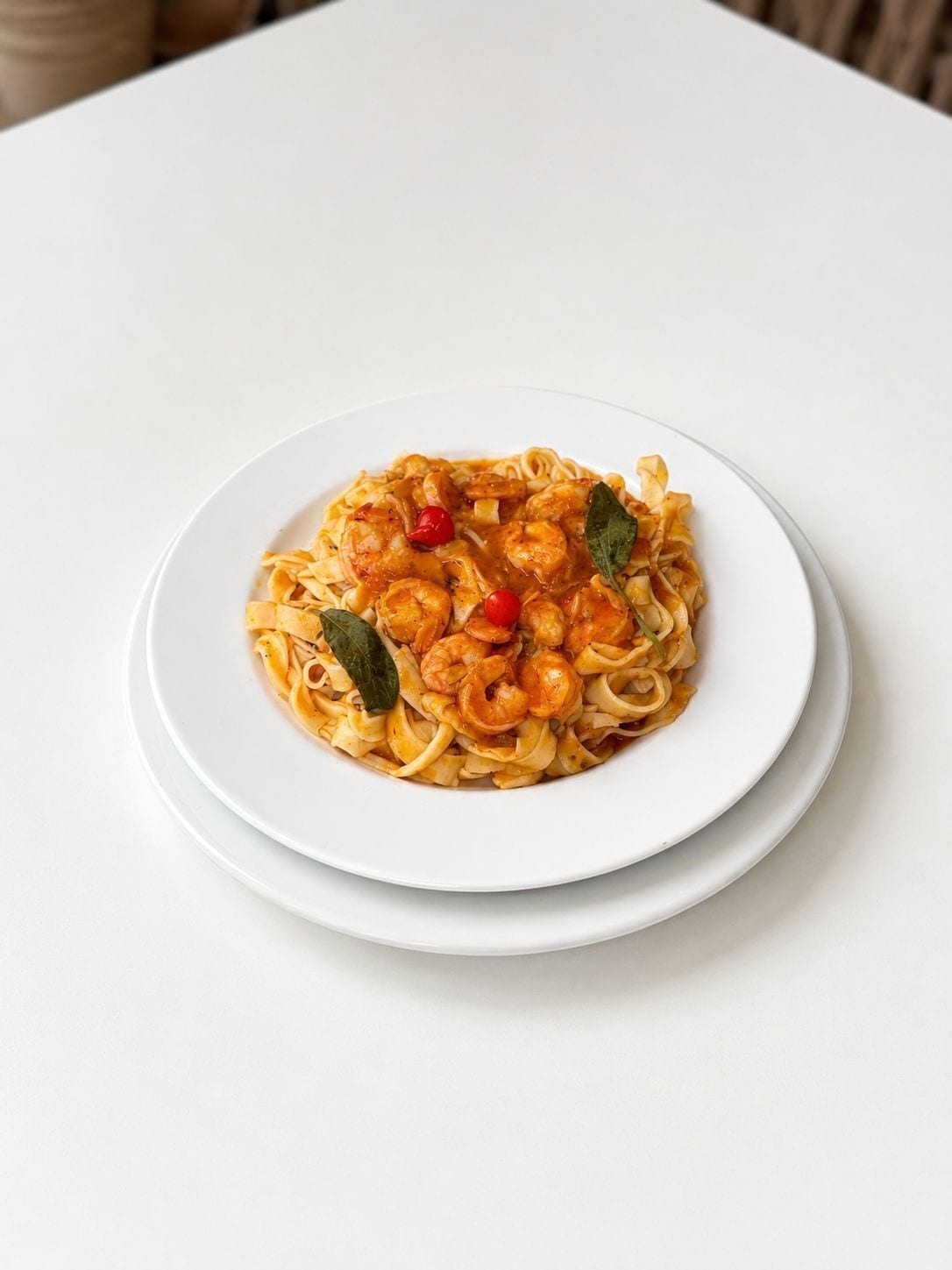 Une assiette de pâtes aux crevettes et aux tomates cerises, servie dans une assiette blanche.