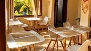 A room with a thatched ceiling, white tables with wooden chairs, and a view of greenery outside. - EstrelaMar Ferradura Pousada, Restaurante & Spa (Búzios)