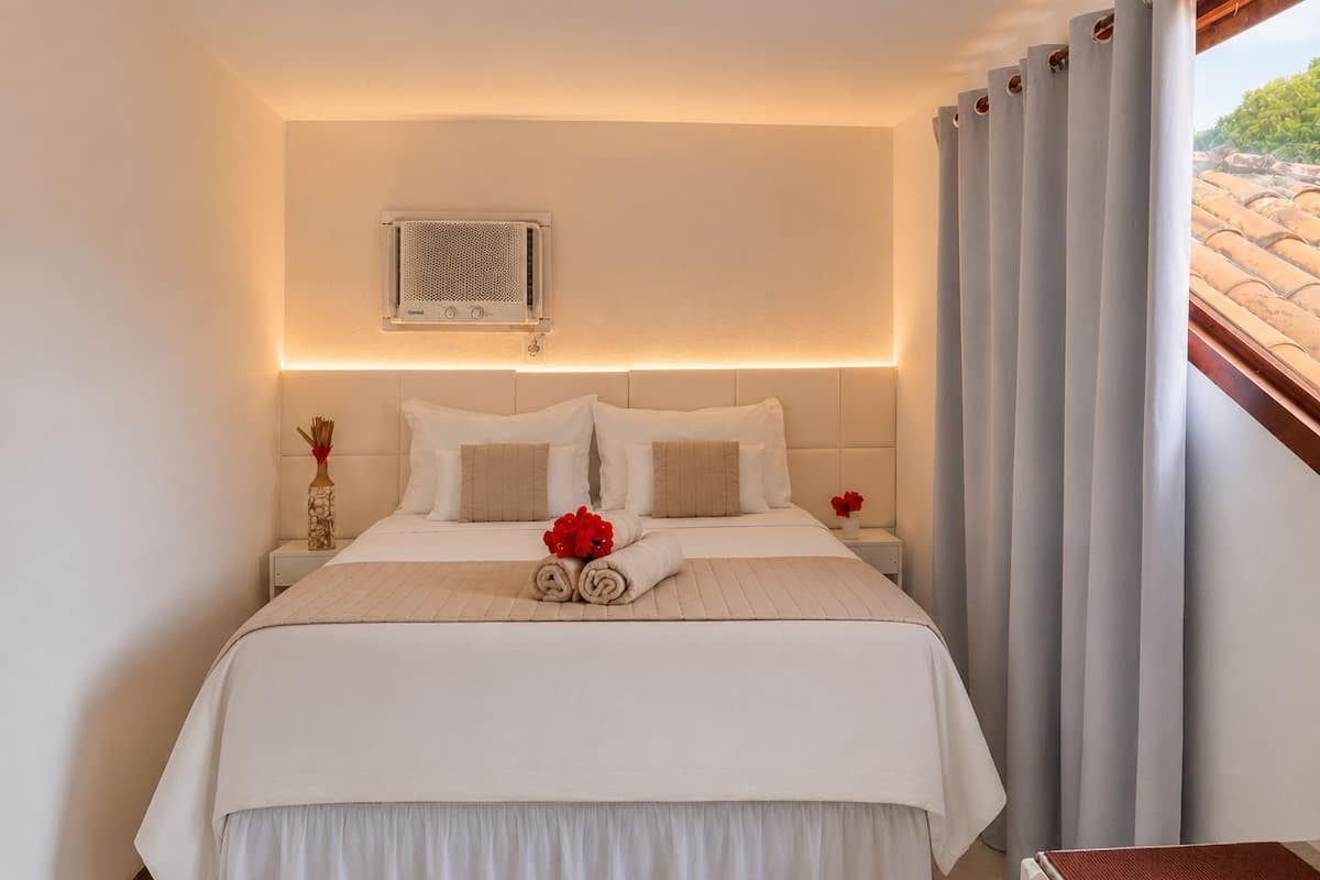 Une chambre d’hôtel avec un lit, une table de chevet, un climatiseur fixé au mur et une fenêtre avec des rideaux.