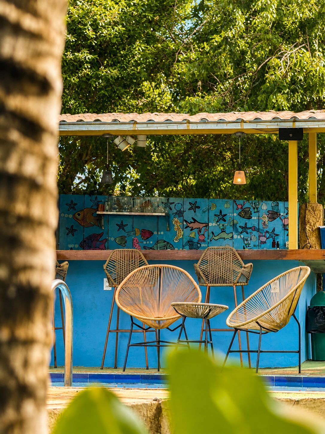 A poolside area with wicker chairs, a tiled wall with fish illustrations, and hanging lights.
